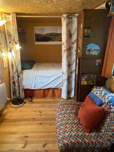 Esta acogedora habitación cuenta con una cama con cortinas, una silla estampada, muebles de madera, almohadas de colores, una lámpara de pie, obras de arte en la pared y una cálida iluminación natural.