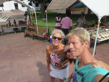 Das Bild zeigt einen Mann und eine Frau, die für ein Selfie vor einem Marktstand posieren, wobei der Arm des Mannes um die Schulter der Frau gelegt ist.