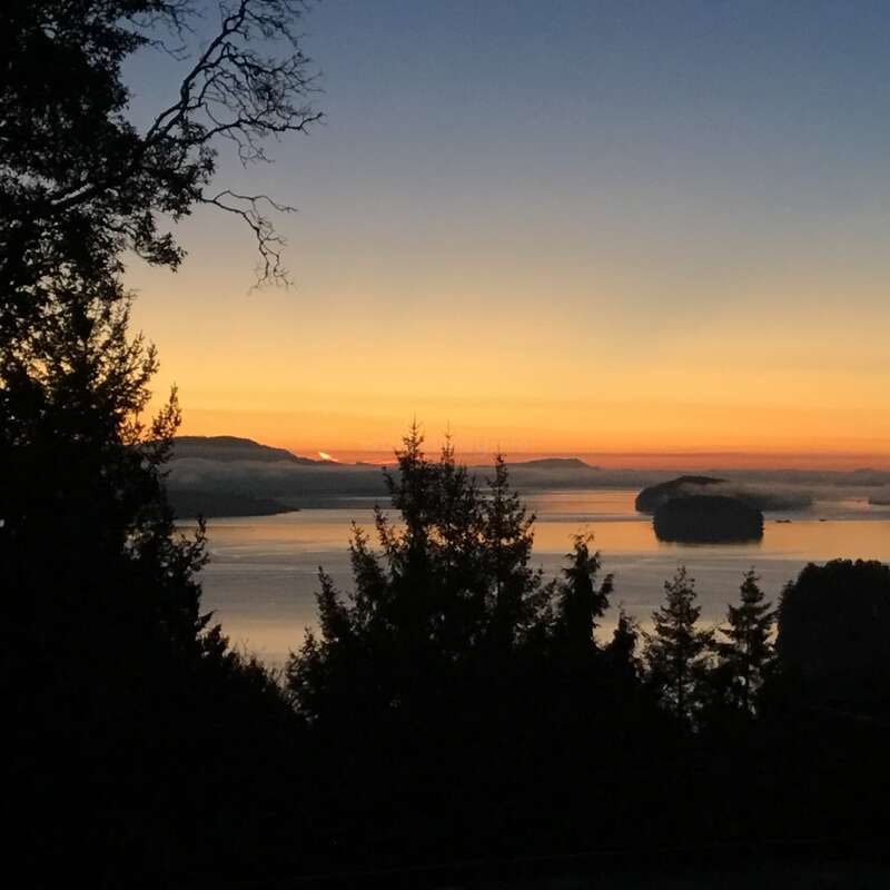 The image depicts a serene sunset over a body of water, featuring silhouetted trees and islands, with a vibrant sky gradating from blue to orange hues.