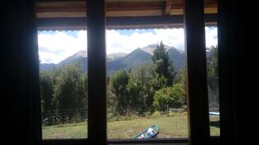 La imagen representa una serena escena al aire libre, con una casa con un gran patio y una pintoresca vista de una masa de agua, probablemente un lago o un río, rodeada de árboles y vegetación.