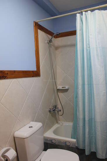 This image shows a small bathroom with a white toilet, a bathtub with a shower, light blue tiles, a blue shower curtain, and pale blue walls.
