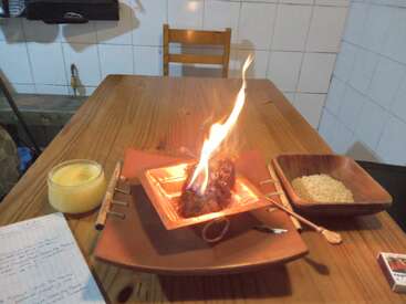 Ein Holztisch mit einem brennenden Gegenstand in einer quadratischen Schale, umgeben von einer Schüssel Reis, einer Kerze, Stiften, einem Löffel und handgeschriebenen Notizen.