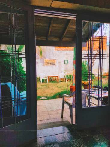 This image captures an inviting backyard view through open glass doors, showing plastic chairs, a table, plants, wall decorations, and a peaceful, homely atmosphere outside.