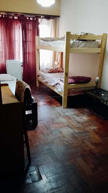 Este quarto aconchegante tem beliches de madeira, uma cama de solteiro, uma mesa com cadeira, cortinas escuras, piso de parquete e uma mesinha de cabeceira com um abajur.