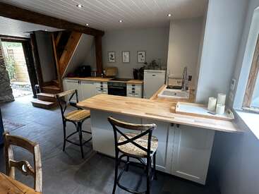 Cette cuisine accueillante se caractérise par des poutres en bois, des armoires blanches, un comptoir en bois, des appareils modernes, des tabourets de bar, des œuvres d'art murales, de grands carreaux et une abondante lumière naturelle provenant des fenêtres.