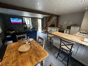 La cuisine et l'espace de vie ouverts et confortables sont dotés de poutres en bois rustiques, de murs en pierre, d'une table à manger en bois, d'appareils électroménagers modernes, d'un canapé et d'une télévision à écran plat.