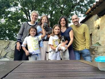 A happy family of six, including two children, poses outside with their pets—a cat and a dog—in a beautiful, natural, and cozy setting. Smiling faces abound.