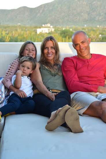La imagen muestra a una familia de cuatro miembros sentados en un sofá blanco al aire libre, con un paisaje montañoso visible al fondo.