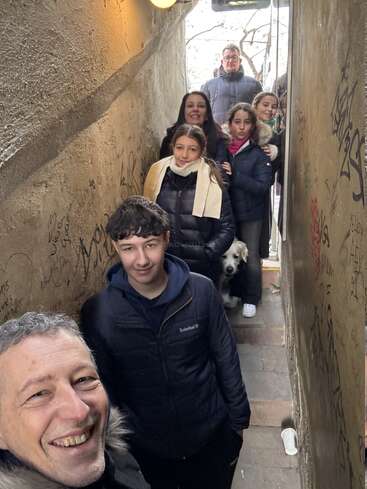 Un grupo de personas, entre las que hay niños y un perro, se apiñan en un callejón estrecho y cubierto de grafitis, sonriendo y posando juntos para hacerse un selfi.