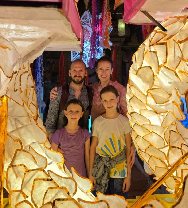The image depicts a family of four posing for a photo, surrounded by vibrant lanterns, with a warm and joyful atmosphere suggesting a special occasion or celebration.