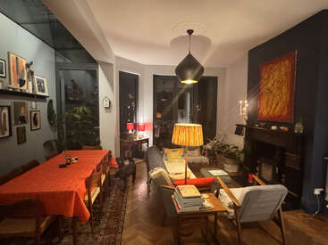 Dieses gemütliche Wohn-Esszimmer besticht durch eine eklektische Einrichtung, warme Beleuchtung, bunte Kunst, Zimmerpflanzen, einen Esstisch mit roter Tischdecke, bequeme Sitzgelegenheiten und Holzakzente.