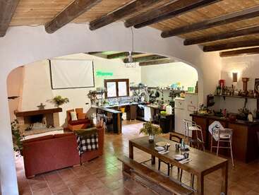 Cette pièce ouverte et confortable comprend une cuisine rustique, un coin repas avec une table en bois, un coin salon avec une cheminée, un bar, des poutres apparentes et une décoration chaleureuse.