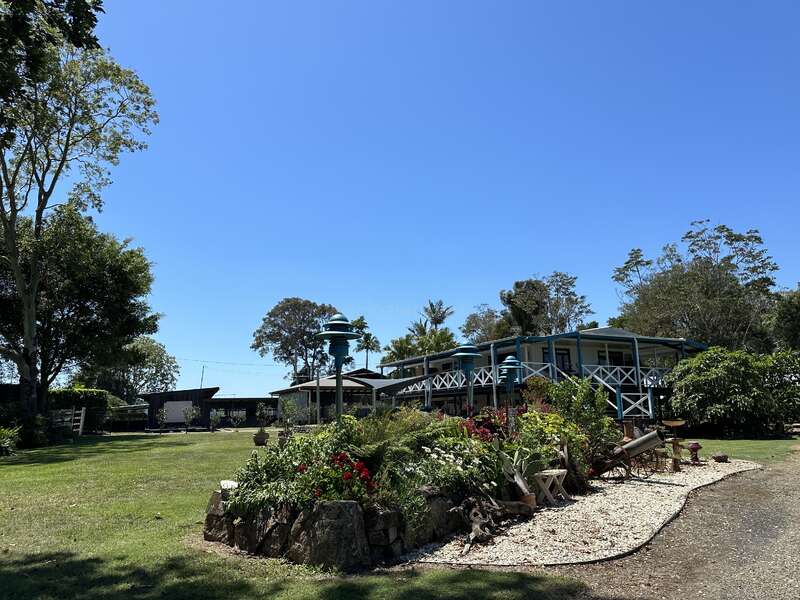 La imagen representa una casa serena con un patio espacioso, con un jardín frondoso, árboles y un cielo azul despejado, que destila tranquilidad y belleza natural.