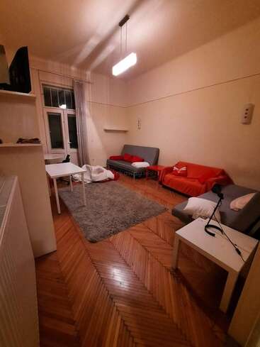 The image depicts a cozy living room with a wooden floor, featuring a couch, rug, table, and chairs, with a window and door visible in the background.