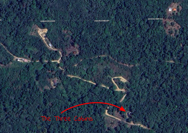 Esta imagen de satélite muestra un denso bosque con carreteras serpenteantes. Una flecha roja con la etiqueta "Las tres cabañas" señala un grupo de edificios entre los árboles.