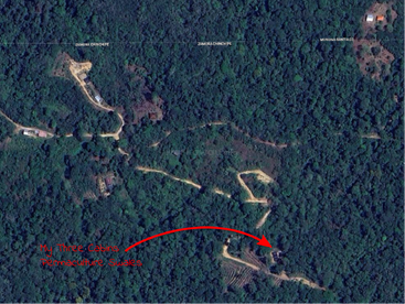 Dieses Satellitenbild zeigt ein bewaldetes Gebiet mit gewundenen Straßen. Ein roter Pfeil zeigt auf Strukturen mit der Aufschrift "My Three Cabins Permaculture Swales". Die Namen der Regionen sind oben zu sehen.