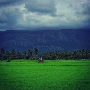 The image depicts a serene landscape featuring a lush green field, a small hut, and a majestic mountain range under a cloudy sky, evoking a sense of tranquility.