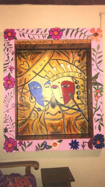 The image features a vibrant painting of two faces on a yellow background, surrounded by a pink floral border, set within a wooden frame.