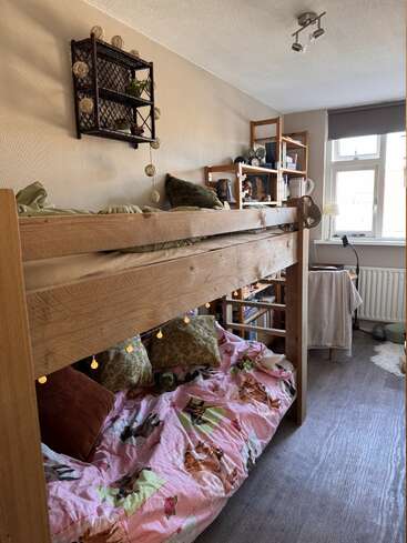 Cette chambre confortable est équipée de lits superposés en bois agrémentés de guirlandes lumineuses, d'oreillers et d'une literie sur le thème des animaux. Des étagères accueillent des objets décoratifs et des livres. Une grande fenêtre laisse entrer la lumière naturelle.