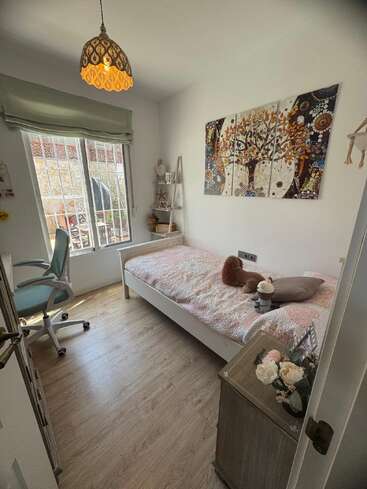 Esta acogedora habitación cuenta con una cama individual, peluches, un cuadro decorativo, un escritorio con silla, una ventana, suelo de madera y una lámpara colgante.