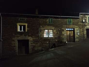The image depicts a stone building with a wooden door, windows, and a chimney, set against a dark night sky, with a subtle watermark in the center.