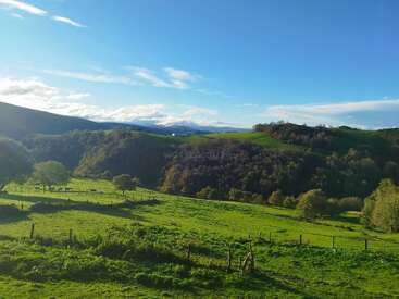 The image depicts a serene landscape featuring rolling hills, lush green grass, trees, and a blue sky with white clouds, evoking a sense of natural beauty and tranquility.