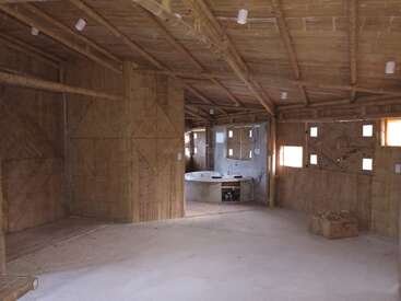Esta imagen muestra el interior de una casa de bambú inacabada con motivos geométricos en las paredes. La espaciosa habitación incluye una bañera parcialmente instalada, pequeñas ventanas y una caja de madera.