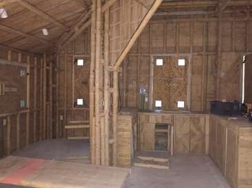 Esta imagen muestra el interior de una cabaña rústica de bambú y madera, con muebles sencillos, vigas a la vista, ventanas pequeñas y tonos terrosos naturales.