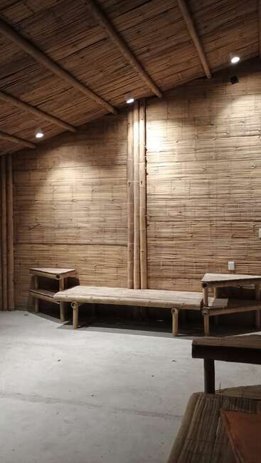 Esta imagen muestra un espacio interior con paredes, techo y muebles de bambú. La iluminación es cálida y crea un ambiente acogedor con texturas naturales y diseño minimalista.