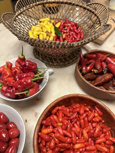 Un assortiment coloré de différents piments est disposé dans des bols et un panier tressé. Les piments rouges, jaunes et verts sont soigneusement rangés, mettant en valeur leur fraîcheur éclatante et leur diversité.