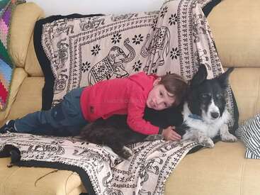 Un chico joven con camisa roja y pantalones azules está tumbado en un sofá con un perro blanco y negro, al que abraza cariñosamente.