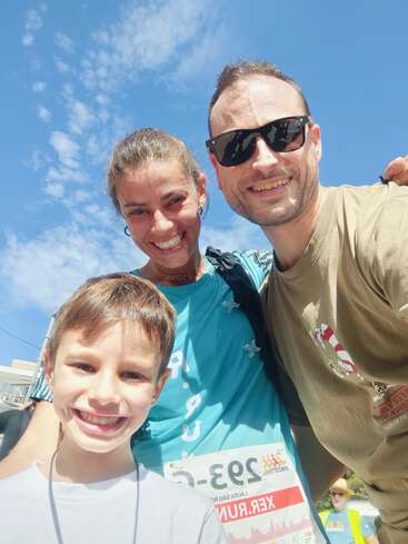 La imagen muestra a una familia de tres miembros posando para una foto, con la madre y el padre a cada lado de su hijo, todos sonriendo a la cámara.
