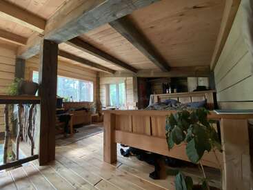 L'intérieur de cette confortable cabane en bois se caractérise par des poutres apparentes, de grandes fenêtres, des plantes d'intérieur et un mobilier rustique. La lumière naturelle remplit l'espace, créant une atmosphère chaleureuse, accueillante et paisible.