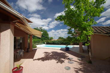 Um quintal tranquilo com piscina, árvore frondosa, pátio com mobília externa e toldo para proteção solar. Os vasos de plantas e o céu azul claro melhoram a atmosfera relaxante.