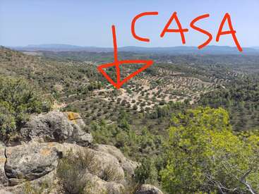 Esta imagem mostra uma ampla paisagem cênica com colinas rochosas, florestas verdes e terras agrícolas. A palavra "CASA" com uma seta vermelha aponta para uma casa distante.