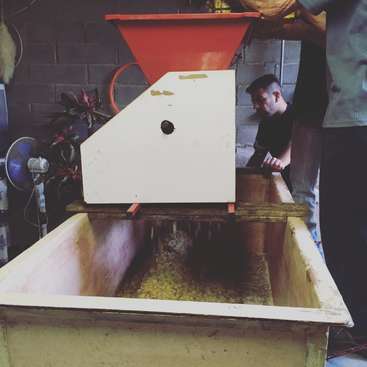 La imagen muestra una gran caja de madera con una máquina blanca y roja encima, probablemente utilizada para procesar o clasificar materiales, sobre un fondo de ladrillos grises.