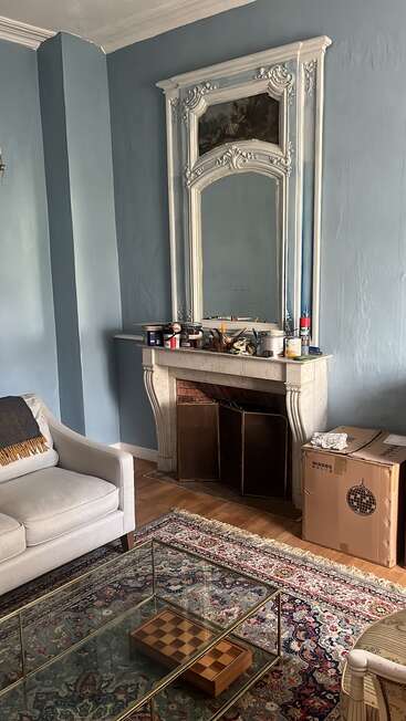 The image depicts a living room with a fireplace, mirror, and couch, featuring a rug, coffee table, and cardboard boxes, with a blue wall and white ceiling.