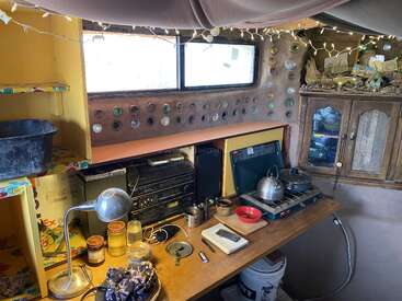 Diese gemütliche, rustikale Küche verfügt über einen hölzernen Tresen, einen Herd, eklektische Dekoration, eine Wand mit Glasflaschen, Lichterketten, Regale, Gläser, eine Stereoanlage, einen Vintage-Schrank und viele kreative Details.