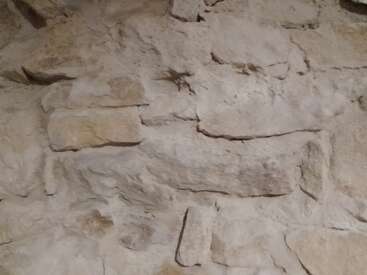 Dieses Bild zeigt eine Nahaufnahme einer rustikalen Steinmauer mit ungleichmäßig geformten, grob gestapelten und zementierten Steinen, die natürliche Texturen und erdige Farbtöne aufweisen.