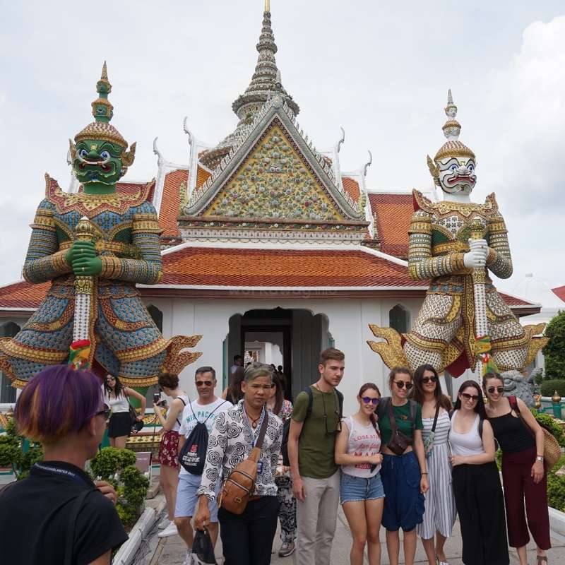The image depicts a group of people standing in front of a temple, with two large statues of mythical creatures flanking the entrance. The temple\'s roof is adorned with intricate designs.