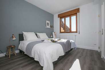 La imagen muestra una acogedora habitación con una cama, un escritorio y una silla, con una estantería y una ventana, que evoca una sensación de comodidad y tranquilidad. La habitación está bien iluminada y es acogedora.