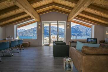 La imagen representa una habitación espaciosa de techo alto, con una gran ventana y suelo de madera, probablemente un salón o una sala de estar, caracterizados por su ambiente abierto y aireado.