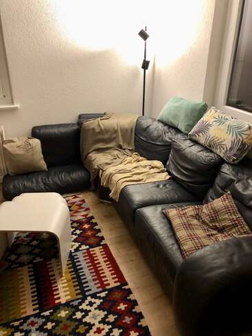 Das Bild zeigt ein gemütliches Wohnzimmer mit einem schwarzen Ledersofa, einem bunten Teppich und einem weißen Couchtisch, der eine warme und einladende Atmosphäre ausstrahlt.