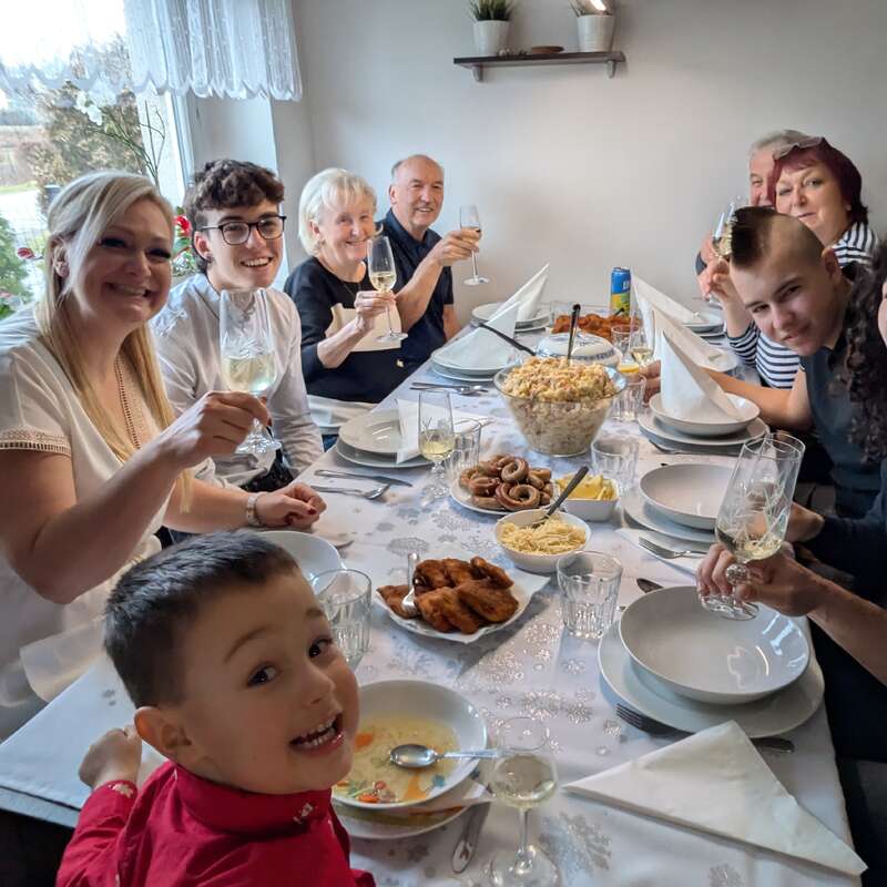 A joyful family gathers around a festive table, sharing smiles, laughter, and a meal together. Plates of food and glasses raised, celebrating togetherness and love.