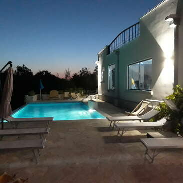 Cette image montre une scène de soirée sereine au bord d'une piscine lumineuse, entourée de chaises longues et d'un bâtiment moderne, avec un magnifique ciel crépusculaire au-dessus de la tête.