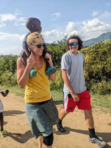 Une femme porte un enfant sur ses épaules alors qu'elle se promène en plein air avec un autre homme. Ils sourient, profitant de la journée ensoleillée sur un chemin de terre.