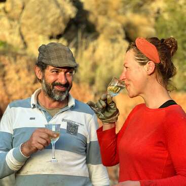 The image depicts a man and woman standing together, each holding a glass of wine, with the woman wearing a red shirt and the man in a blue and white striped shirt.