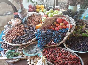 A rustic table overflows with colorful fruits, vegetables, eggs, nuts, dried herbs, pinecones, and berries, creating a vibrant, abundant display of natural, healthy harvest.