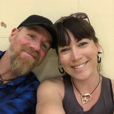 The image shows a man and woman posing for a selfie, with the man on the left and the woman on the right, both smiling at the camera.