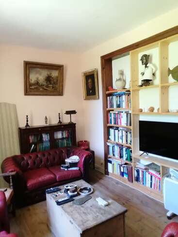 Esta aconchegante sala de estar tem sofás de couro vermelho, piso de madeira, estantes cheias de livros, uma TV, obras de arte, esculturas e uma mesa de centro rústica de madeira.